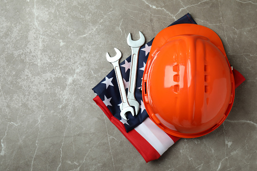 American flag with hard hat and wrenches on gray textured background