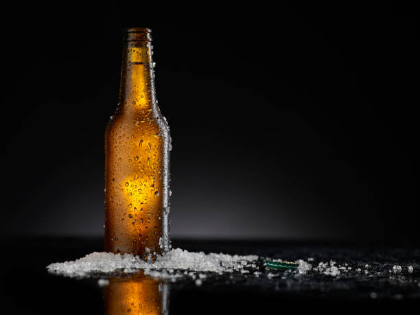 istock Ice Cold Brown Beer Bottle Covered with ice and water drops - condensation. Blank for drink beverage product design mock-up.  Standing on black table with dark - black background. 1310049898