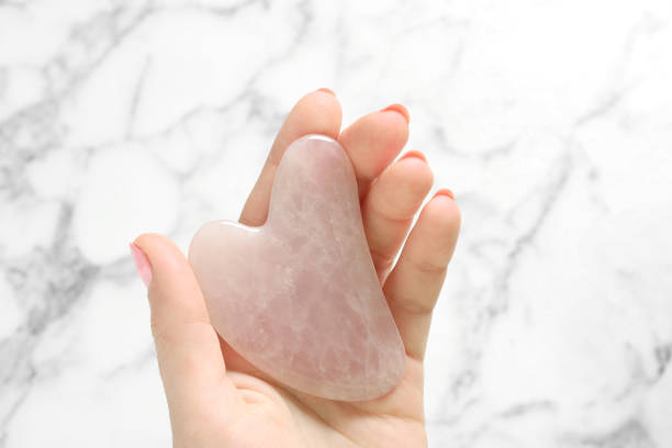 istock Woman with rose quartz gua sha tool at white marble table, top view 1310051103