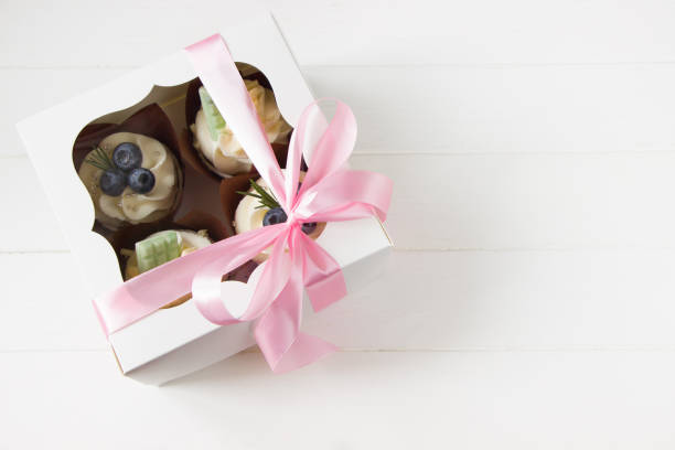 istock Cupcakes  with cream cheese and fresh blueberries, white paper box with pink bow,  white background. Berry cupcakes in delivery box. Sweet food delivery 1310054533