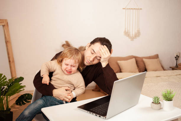 男はラップトップで自宅で働いています。子供はヒステリックに叫ぶと仕事の気晴らしを防ぎます。父親は、怒って、疲れて、彼の娘に対処することはできません。コンピュータ内部でフリ� - mother baby child playing ストックフォトと画像