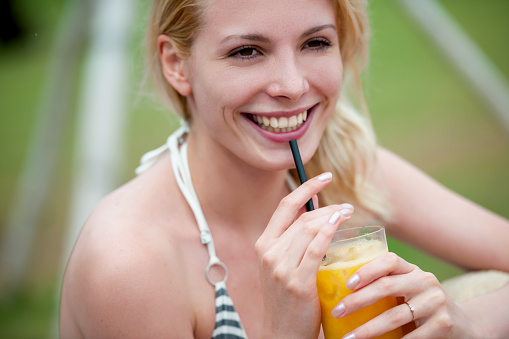 Cheerful young woman drinks juice outdoors