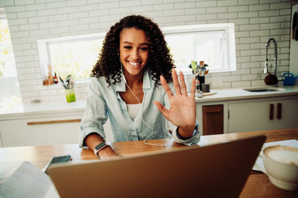 istock Mixed race female student waving on video call typing on laptop sitting in kitchen 1310055680