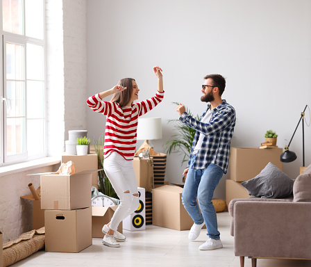 Full body side view of delighted young man and woman jumping happily while having fun during moving into new apartment