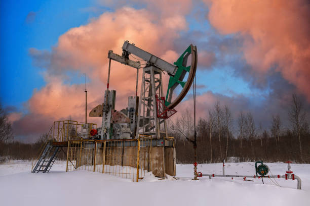 Oil pump jack winter working. At the orange sunset dawn of the sky with clouds. Oil rig energy industrial machine for petroleum in the sunset background for design. Nodding donkey la bomba de aceite jack el invierno funciona. en el amanecer de la puesta de sol naranja del cielo con nubes. máquina industrial de energía de plataformas petrolíferas para petróleo en el fondo de la puesta del sol para el diseño. burro asintiendo con