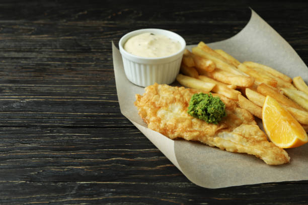 istock Baking paper with fried chips and fish on wooden background 1310060550