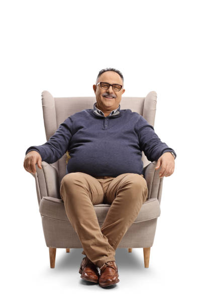 Happy mature man sitting in an armchair and smiling Happy mature man sitting in an armchair and smiling isolated on white background chubby arab stock pictures, royalty-free photos & images