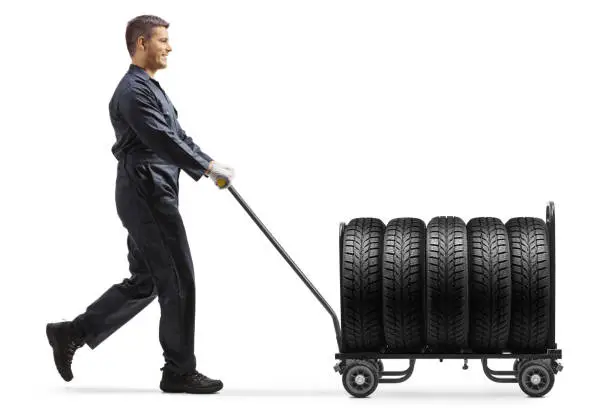 Worker in a uniform pushing vehicle tires on a hand truck isolated on white background