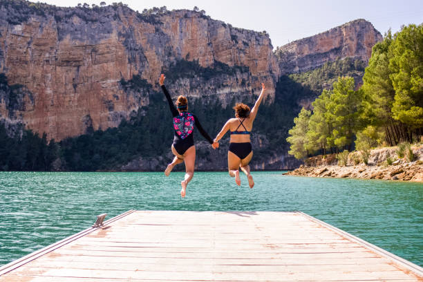 Rear view of two women jumping into the water from a jetty Rear view of two women jumping into the water from a jetty people jumping sea beach stock pictures, royalty-free photos & images