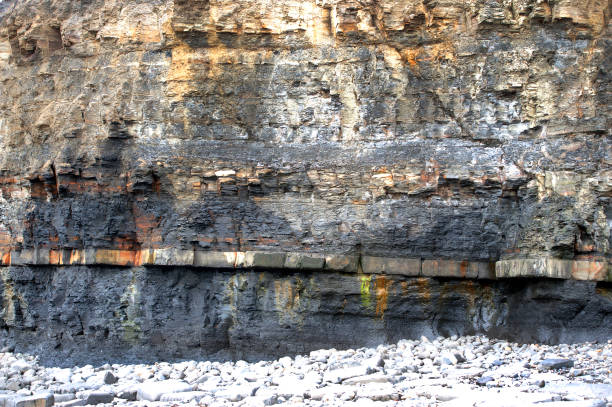 A multitude of colours in the Kimmeridge Shales oil bearing rock on a bleak day where no people venture along the coastline with moody sky and cliff strata along the wave swept waters edge in this beautiful scenery in Kimmeridge Bay, part of the coast that is open to the public as footpaths and trails along the Jurassic Coast, Dorset, England, UK