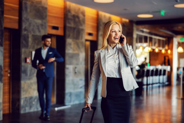 szczęśliwa bizneswoman w podróży służbowej spaceru w holu hotelu i rozmowy przez telefon. luksus, biznes, telekomunikacja, biznes pierwszy,euforia - arrival departure board airport travel business travel zdjęcia i obrazy z banku zdjęć