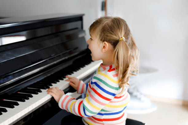 リビングルームでピアノを弾く美しい小さな幼児の女の子。ホームスクーリングコロナウイルスロックダウン中に学習コンセプトで楽器を演奏することを学んで楽しんでいるかわいい就学前� - piano keyboard instrument one person piano key ストックフォトと画像