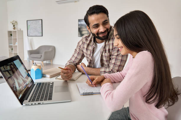 felice ragazza della scuola indiana che si diverte durante la lezione virtuale con l'apprendimento a distanza degli insegnanti online a casa. studentessa figlia adolescente che studia lezione di homeschool remota su computer portatile con padre - home schooling foto e immagini stock