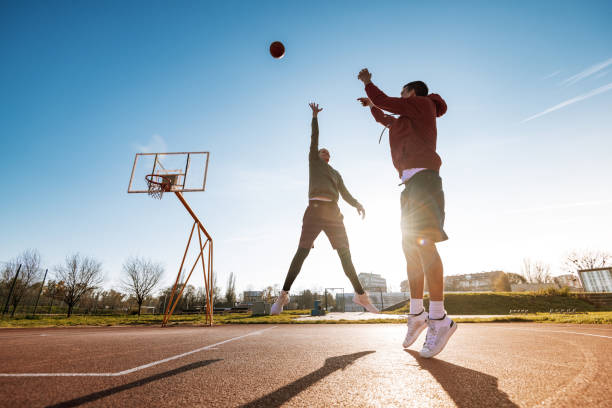 Man and woman playing basketball outdoors, man doing a slam dunk