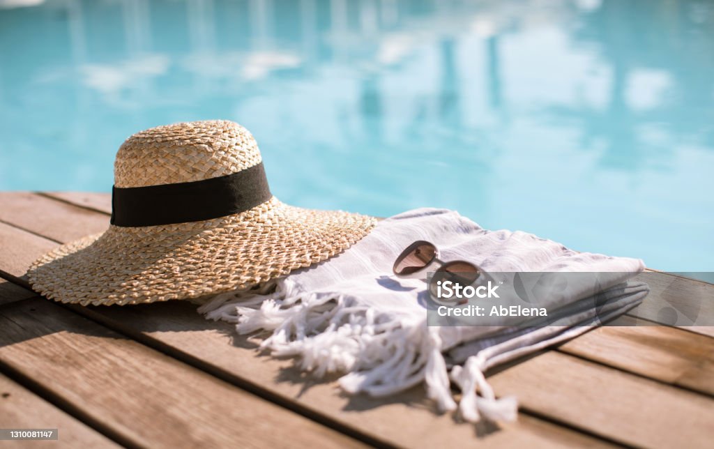 Sunglasses and straw hat Sunglasses and straw hat on the wooden floor at the pool. Summer Vacation Fashion Concept. Swimming Pool Stock Photo