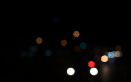 Colored circles bokeh of car lights at black dark night in city. Blurry abstract texture background.