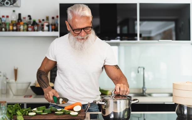 Happy senior man having fun cooking at home - Elderly person preparing health lunch in modern kitchen - Retired lifestyle time and food nutrition concept Happy senior man having fun cooking at home - Elderly person preparing health lunch in modern kitchen - Retired lifestyle time and food nutrition concept fashionable dad stock pictures, royalty-free photos & images