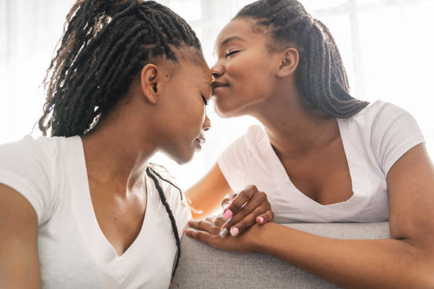 istock Mother and daughter sitting on sofa at home give kiss on forehead 1310089430