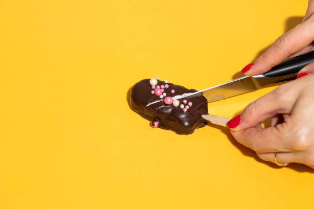 istock Cutting a marshmallow in chocolate on a stick with a knife. Yellow background with space for text. Selective focus. 1310093284