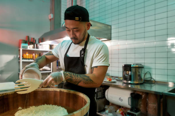 istock Young male chef cook adding vinegar while making sushi rice in a wooden barrel in the kitchen of Japanese restaurant 1310094886