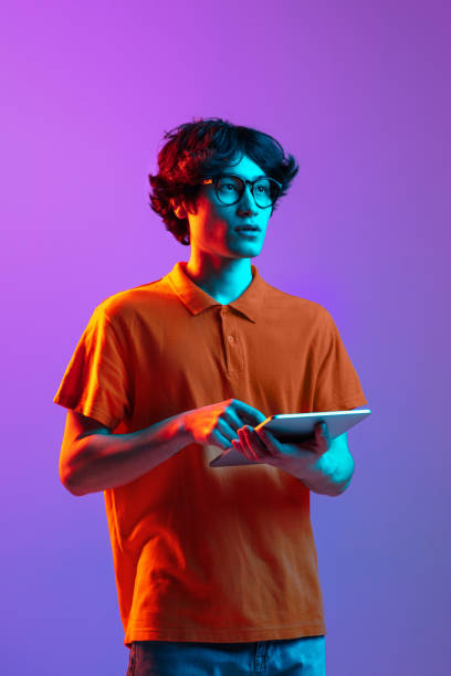 istock Young man in glasses with device isolated on gradient background in neon 1310095070