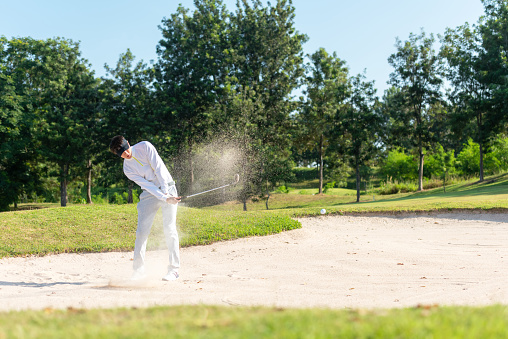 Asia Golfer man hitting out of a sand trap. The golf course is on the sand.  Hobby in holiday and vacations on club golf. Lifestyle and Sport Concept