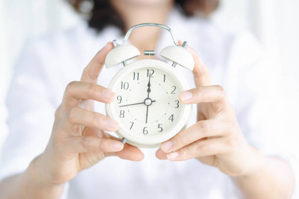 istock Closeup hand holding alarm clock on white bed, Time to wake up 1310097214