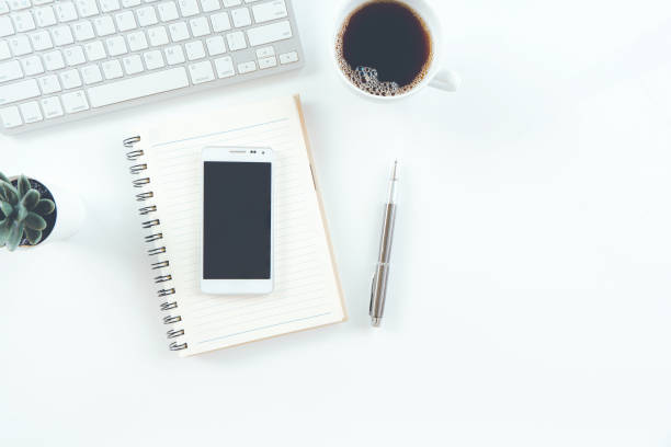 istock Modern white office desk table with laptop computer, smartphone with black screen over a notebook and cup of coffee. Top view with copy space, 1310102010
