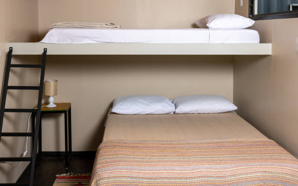 istock Internal view of a hostel type hostel with a bed suspended another bed at floor level. In detail stairway to climb and lamp to the left corner. Three pillows and a red bedspread. 1310102045