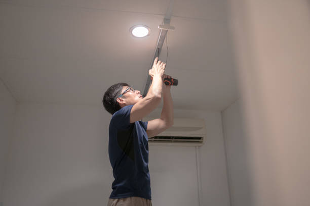 Asian Chinese electrician man installing electric lamp on ceiling using cordless drill.
