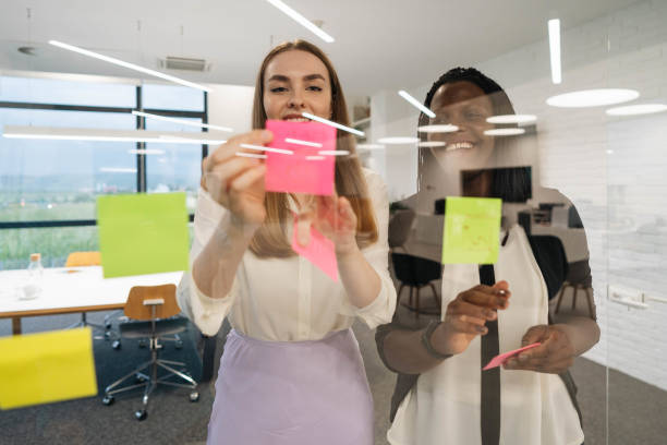 istock Smiling businesswoman writing notes on sticky papers on glass wall 1310103165