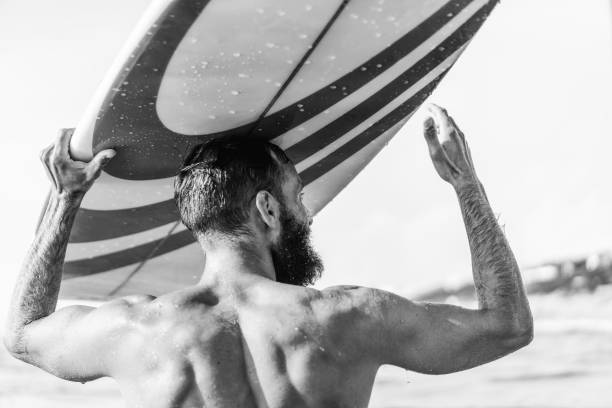 istock Young hipster man with surfboard on his head greeting friends with a gesture - Guy having fun doing extreme sport - Sporty bearded man training with surfboard on the sea - Lifestyle, freedom concept 1310104684