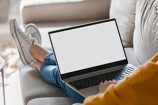 Young woman using laptop screen blank, mock up lying on the sofa at home
