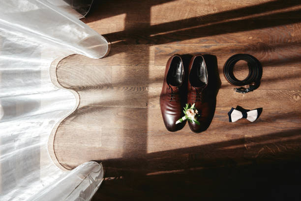 feche acima de sapatos marrons masculinos, gravata borboleta, cinto e boutonniere no fundo do chão de madeira, espaço de cópia. acessórios modernos do homem. detalhes do casamento - shoe groom wood luxury - fotografias e filmes do acervo