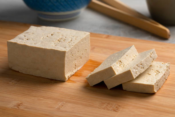 morceau de tofu frais et tranches sur une planche à découper - tofu photos et images de collection