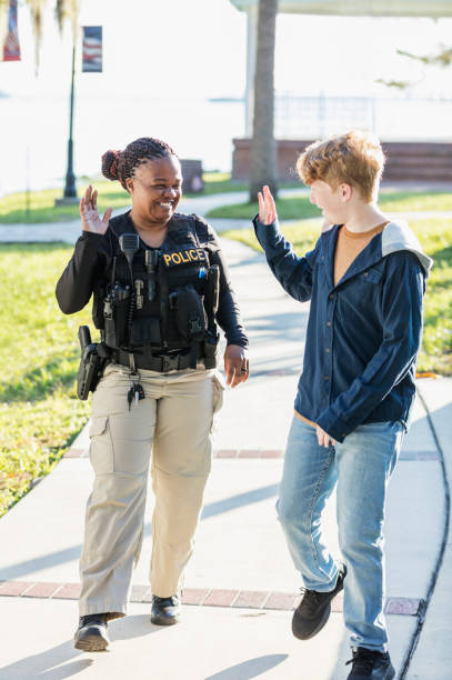 Policewoman greeting boy as he walks by Community policing - a female police officer smiling and waving to a boy as he greets her and walks by. The policewoman is a mature African-American woman in her 40s. The boy is 12 years old. female police officer stock pictures, royalty-free photos & images