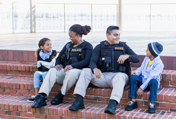 Two police officers in community, sitting with children Community policing - two police officers hanging out with two young children, sitting side by side on steps outside a building. The officers are an African-American woman in her 40s and an Hispanic man in his 20s. The children are brother and sister, 8 and 7 years old, mixed race African-American and Caucasian. female police officer stock pictures, royalty-free photos & images