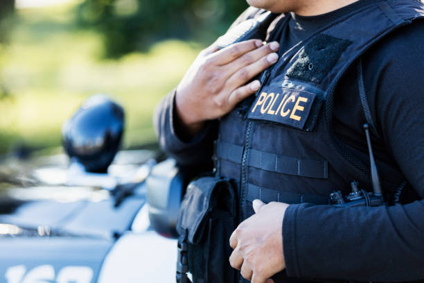 Cropped view of police officer Cropped view of a young Hispanic police officer standing outside his patrol car. midsection photos stock pictures, royalty-free photos & images
