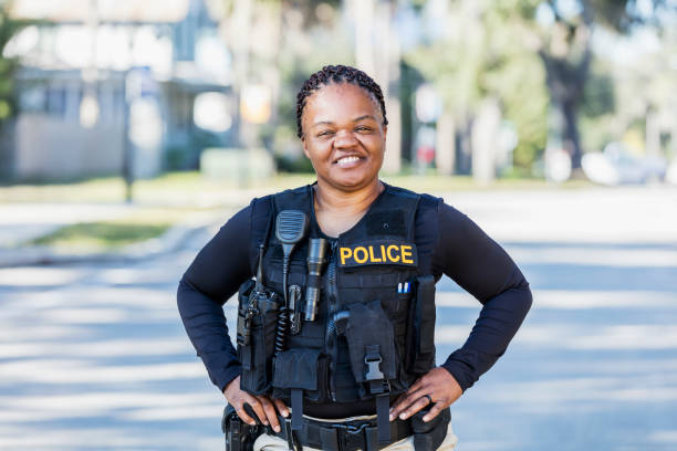 African-American policewoman on foot patrol Community policing - an African-American police officer patrols a local neighborhood on foot. She is a mature woman in her 40s, smiling at the camera with her hands on her hips. police force stock pictures, royalty-free photos & images