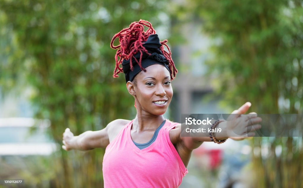 African-American woman doing yoga outdoors An African-American woman in her 30s practicing yoga outdoors. She is smiling at the camera, arms outstretched in a warrior pose. African-American Ethnicity Stock Photo