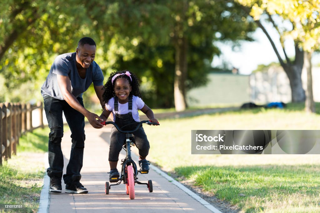 Front view father helps excited little girl riding tricycle Cycling Stock Photo