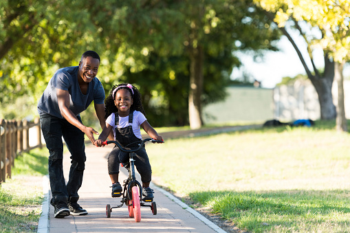 Smiling little girl riding tricycle with father in park