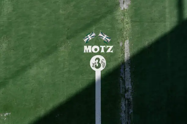 fronton wall in the Basque sport of ball, in which the game marks with the number 3 are painted Above the number 3 there are two Basque flags and the word, Motz, loose, not strong enough, painted in negative in a white circle on a green background