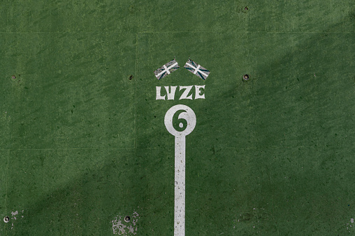 fronton wall in the Basque ball sport, in which the game marks with the number\n 6 Two Basque flags appear above number 6 and the word, Luze, strong, in Basque, not strong enough, painted in negative in a white circle on a green background