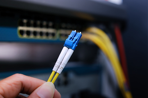 Close up fiber optic cable and blur network router switch on background in a technology data center room. ST-LC Patch Cord