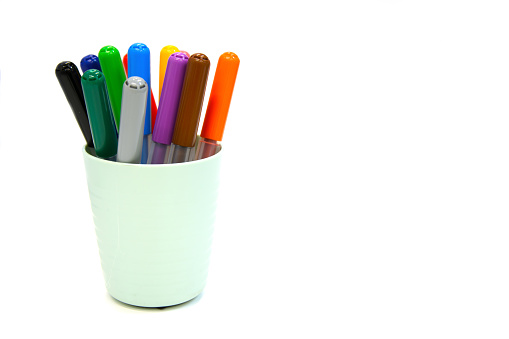Multi colored markers in plastic cup isolated on a white background. Materials for children's creativity, drawing, sketching. Space for text.