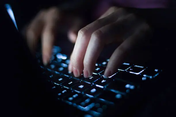 Close-up shot of female hands typing on computer keyboard, working late at home.