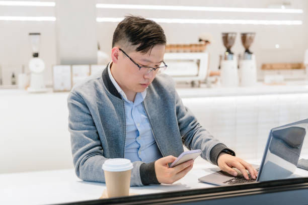 istock Young asian man using laptop and smartphone while working from cafe 1310123222