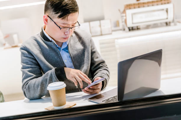 istock Young asian man using laptop and smartphone while working from cafe 1310123299