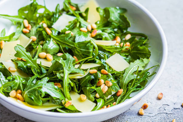 Arugula and parmesan salad with pine nuts in white bowl, close up. Italian cuisine concept. stock photo
